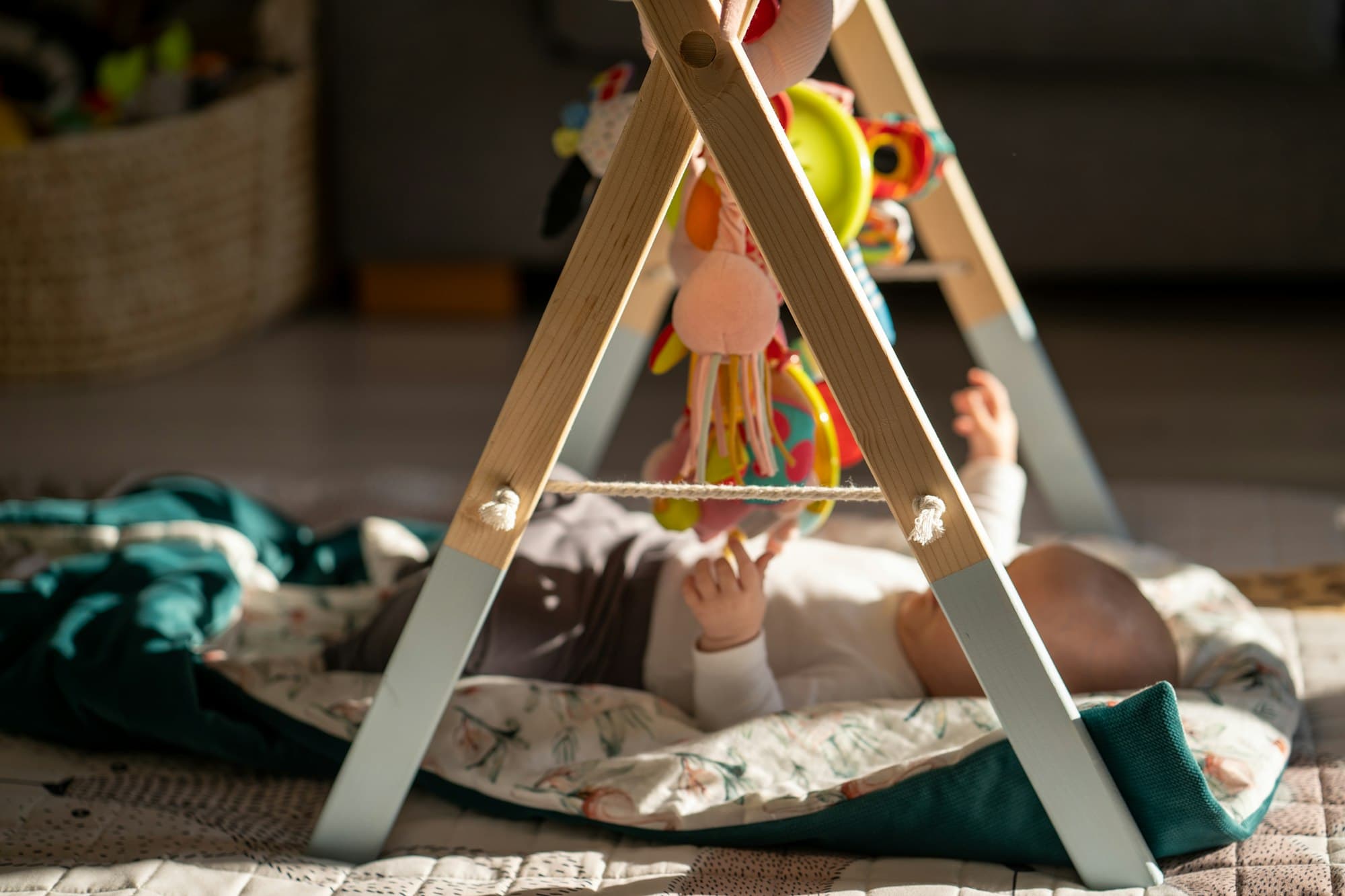 A baby playing under a wooden play frame